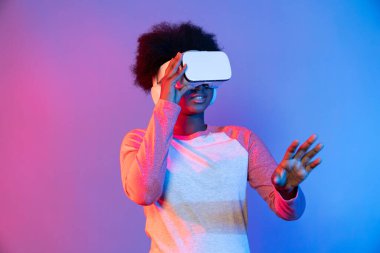 Genç Afrikalı, teknolojik dijital yenilik grafiğinde mavi neon aydınlatma grafiğinde izole edilmiş 3 boyutlu hologram veri uygulamasını seçmek için metaevren üzerinden VR gözlük takıyor. Entrika.