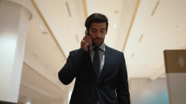 Profesyonel bir iş adamı yürüyen merdiven kullanırken telefonla konuşuyor. Beyaz tenli yönetici, pazarlama fikri ya da planı rapor etmek ve tartışmak için iş ekibiyle konuşuyor. Ön manzara. Sevinçli..