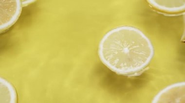 Dalgalı su yüzeyinde limon dilimleri. Sarı arka planda ve su dalgasında dilimlenmiş limon dilimini kapat. Doğal ışık. Makro. Tazelik ve susuzluk kavramı. Poster için tasarım, tebrik kartı. Pabulum.