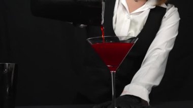 Makrografi, bir barmenin martini bardağına canlı kırmızı bir kokteyl karıştırma sanatına tanık olmak, güzel süslenmiş taze bir biberiye ve parlak siyah bir arka plan. Geliştirilebilir.