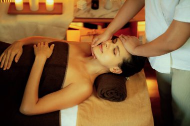 Beyaz kadın stres önleyici kafa masajı yapmaktan ve lüks otel veya otelde sıcak mum ışığında yüz güzelliği eğlencesi yapmaktan zevk alıyor. Sessiz.