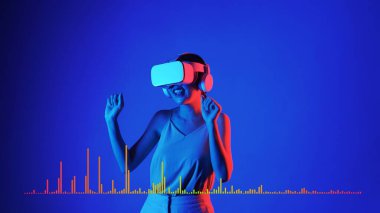 Müzik ve teknoloji konsepti mavi arka planda, stüdyo dinamik ışıklandırmasında VR kulaklıkla müzik dinleyen ve dans eden gülümseyen kadın. Halüsinasyon.