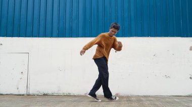 İspanyol adam kollarını açıp duvarın önünde dans ediyor. Modern dansçı ya da koreografın, günlük kıyafetleriyle hip hop stiliyle dans ederken ki hareketli çekimi. Açık hava sporu 2024. ÇalışmaComment.