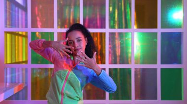 Neşeli İspanyol kız gece kulübünde renkli giysiler giyerken neon ışıkta müzik eşliğinde hareket ediyor. Sokak dansçısı kameraya bakarken hareketli adımlar atıyor. Mutluluk.