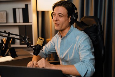 Sunucu kanalı akıllı yayıncı laptopta canlı sosyal medya uygulaması arıyor, kulaklık takıyor ve modern ofis stüdyosundaki mikrofonu kullanıyor. Bireysel.