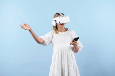 Kafkasyalı bir kız elinde telefon tutarken ve görüş açısını gösterirken VR gözlük takıyor. Görsel gerçeklik dünyasını ya da metaevreni keşfetmek isteyen mutlu kadın şaşırdı. Teknoloji yeniliği. Kısıtlanma.