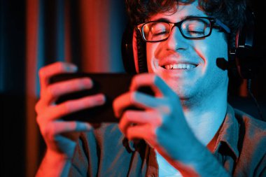 Gülümseyen genç oyun flaması takımı Esport ile online olarak akıllı telefon dövüşlerinde neon ışıklı odada kulaklık takarak oynuyorlar. Bir sonraki aşama için rakipleri kazanmak için strateji planı uyguluyorum. Toplayıcı.