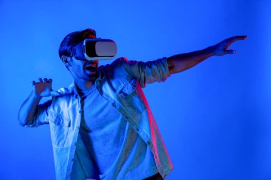 Mutlu adam hareketli voleybol hareketini yaparken neon arka planda VR cam kullanıyor. Beyaz tenli genç ve oyuncu gözlük ve yenilik teknolojisi ile spor oyunu oynuyorlar. Sapma.