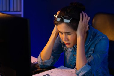 Stresli, genç, güzel Asyalı yaratıcı proje yaratıcısı sosyal medyayı araştırmak için bilgisayara bakıyor ve geceleri daha çok neon modern ofisin planlama kanalı stratejisine ulaşılıyor. Taktik.