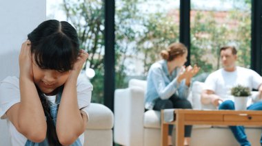 Stresli ve mutsuz genç kız köşeye kıvrılıp kulaklarını kapatarak arka planda ebeveyninin tartışmasını engelliyor. Evde aile içi şiddet ve travmatik çocukluk depresyona dönüşür. Eşzamanlama