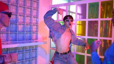 Ortasında dans eden profesyonel mutlu hipster onu alkışlayan çeşitli arkadaşlarıyla dans ediyor. Çekici Asyalı kırığı gece kulübünde neon ışığıyla enerjik adımlar atıyor. Mutluluk.