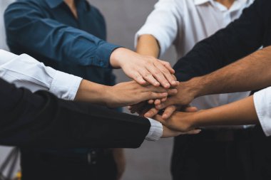 Çeşitli ofis çalışanlarından oluşan bir grup, ofis odasında el ele vererek iş sinerjisini ve iş yerindeki güçlü verimli takım çalışmasını sembolize ediyor. İş çalışanları arasındaki işbirliği ve birlik. Tedbirli