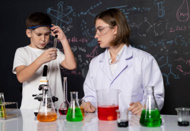 Öğretmen, laboratuarda öğrenciyi destekliyor. Öğrenci ve öğretmen cam kapta sıvı kullanarak STEM sınıfında kimya bilimi üzerine deney yapıyorlar. Karıştırma çözeltisi. Etkinlik.