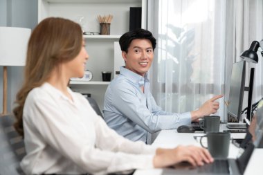 Gülümseyen Asyalı bir adam, yan görüntüdeki modern ofis çalışma masasında veri tabanını ararken günlük dizüstü bilgisayarla pazarlama raporu projesini planlarken kadın meslektaşıyla konuşuyor. İnfobahn.