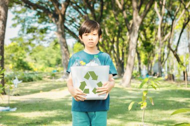 Neşeli Asyalı çocuk, elinde gündüz vakti elinde geri dönüşüm sembolü olan yeşil parkı tutarak atık geri dönüşümünü teşvik ediyor, azaltıyor ve gelecek nesiller için sürdürülebilir çevre farkındalığı için teşvikleri yeniden kullanıyor. Döngü