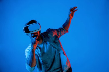 Sanal programı keşfetmek ve girmek için VR gözlük takan heyecanlı bir adam. Yetenekli oyuncular metaevrene dokunurken gündelik giysiler giyer ve neon ışıklı arka planda dururlar. Yaşam tarzı. Sapma.