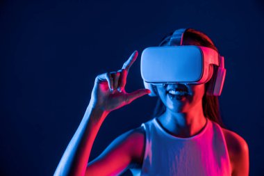Etrafı neon ışıklı kulaklıklarla çevrili bir kadın metaevreni bağlayan VR kulaklık takıyor, fütüristik siber uzay topluluk teknolojisi yayıyor, işaret ve başparmak ile sanal nesne etkileşimi kuruyor. Halüsinasyon.