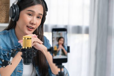 Asyalı sunucu canlı yayında canlı yayında canlı yayında sosyal medyada kulaklık takarak konuşuyor. Dinleyicileri modern stüdyoda koçluk yaparak selamlıyor. Taktik.