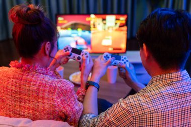 Kontrollü joystickli birkaç oyuncu, televizyon ekranında birlikte araba yarışı oyunu oynuyorlar. Arka tarafta atıştırmalıklar, modern konforlu evinde neon ışıklı oturma odasında kanepe. İnfobahn.