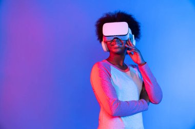Profil, VR gözlük takan genç ve güzel Afrikalıların mavi ve pembe neon ışıklı arkaplanda izole olduğunu düşünüyor. Teknoloji ve dijital yenilik 3 boyutlu hologram gramında. Entrika.
