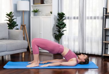 Spor kıyafetleri içinde esnek ve becerikli bir kadın evde egzersiz paspası üzerinde meditasyon pozisyonunda yoga yapıyor. Huzurlu ve huzurlu bir yoga yaşam tarzı..