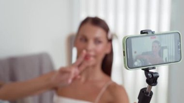 Genç sosyal medyum kadın moda videosu yapıyor. Blogcu kameraya selfie çubuğu ve ışık halkası kullanarak gülümserken, aynı zamanda ikna edici çevrimiçi kıyafetlerin izleyicilere veya takipçilere vlog satmasını sağlıyor. Düzenle