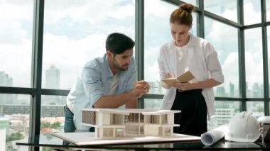 Beyaz mimar mühendis takımı ev modelini ölçmek için birlikte çalışıyor. Genç, güzel tasarımcı ev inşaatı yazarken erkek işçiler mimari modelleri inceliyor, inceliyor, inceliyor. Tartışma