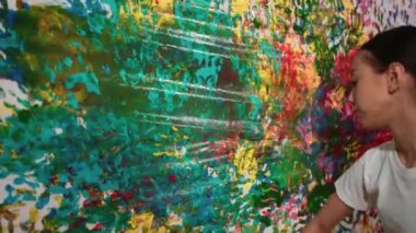 Genç mutlu kız renk tepsisini tutuyor ve fikri ifade etmek ve el iziyle hayal gücünü geliştirmek için renkli duvarları boyuyor. Resim dersinde odayı dekore etmek için beyaz kız pulu. Öğretim