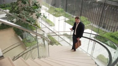Mutlu iş adamı başarılı projesini ve menajerini akıllı telefon kullanarak kutluyor. Erkek lider, modern binada merdivenlerde dururken telefonla pazarlama ekibini konuşuyor. Urbane.