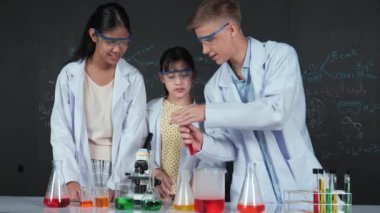 Zeki çocuk deney yaparken deney kabında sıvı karıştırıyor. Akademik öğrenci laboratuvar önlüğü giyerken masada mikroskop ve deneysel ekipmanlarla renkli örnekler koyuyor. Öğretim