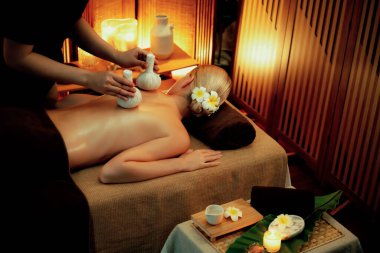 Sıcak bitkisel top spa masaj vücut tedavisi, masör kadın vücuduna nazikçe şifalı bitki torbası bastırıyor. Aromaterapi tesisinin sakinliği ve dinginliği kaplıca salonundaki mumların sıcacık ışığında. Sessiz.