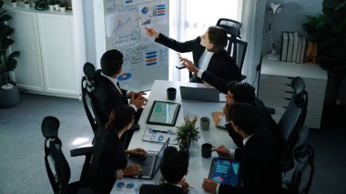 Akıllı yönetici projesinin üst görünümü beyaz tahtaya zihin haritası ve finansal grafik ile işaret ediyor ve çeşitli yatırımcılar hisse yatırım grafiğini dinleyip analiz ederken pazarlama fikrini açıklıyor. Müdürlük.