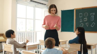 Beyazca öğretmeni, ilkokulda karatahta başında dururken vücut jesti kullanarak çok kültürlü öğrencilere teoriyi öğretiyor ve açıklıyor. Yetenekli öğretmen çocuklara soru soruyor. Pedagoji.