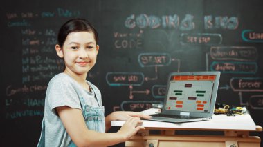 Asyalı öğrenci mühendislik kodları ya da masadaki ekipmanlarla birlikte kameraya doğru dönün. Güvertede dizüstü bilgisayar kullanarak çalışan tatlı bir kız. Yaratıcı eğitim konsepti. Öğretim.