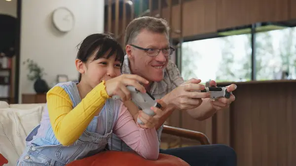 stock image Grandfather and granddaughter together play console game, entertainment media. Old senior use technology communicate with new generation kid cross generation gap strengthen family bond. Divergence.