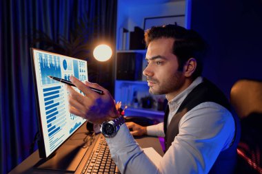 Akıllı işadamı, gece vakti mor neon ışıklı ev ofisin bilgisayar ekranında hizmet ürün veritabanındaki araştırma hedef pazarına odaklanmak için masa başında kalemle işaret ediyor. Tahmin et..