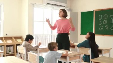 Beyazca öğretmeni, ilkokulda karatahta başında dururken vücut jesti kullanarak çok kültürlü öğrencilere teoriyi öğretiyor ve açıklıyor. Yetenekli öğretmen çocuklara soru soruyor. Pedagoji.