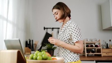 Kafkasyalı anne, modern mutfakta dizüstü bilgisayarda yemek tarifine bakarken salata yapmak için yemek hazırlıyor. Yetenekli ev bekçisi taze sebze kullanarak kahvaltı hazırlıyor. Pedagoji.