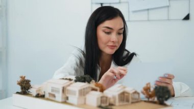 Genç ve güzel mimarın yakın çekimi mimari modeli ölçerken, modern toplantı odasındaki masadaki planlar ve mimari modeller arasında karşılaştırma yapıyor. Yaratıcı tasarım konsepti. Tertemiz..