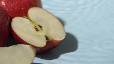 Mavi arka planda dilimlenmiş kırmızı elmaları kapatın. Elma dilimlenmiş makarnanın mavi arka planında elmacı ve suyun dökülmesi ve el sallaması. Sağlıklı beslenme ve taze üretim kavramı. Pabulum.