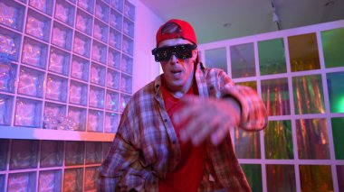 Yakışıklı, beyaz tenli sanatçı kurşun ışıkla dans etmek için dans ediyor. Güneş gözlüklü, şapkalı çılgın hippi dans ediyor ve modern gece kulübünde serbest dans dinlemenin tadını çıkarıyor. Mutluluk.