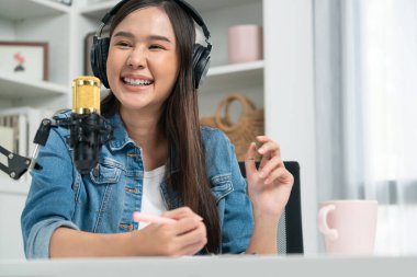 Sosyal medyada kulaklıkla canlı yayın yapan Asyalı sunucu modern stüdyoda yaşam koçluğu veya pazarlama dinleyicilerini selamlıyor. Taktik.