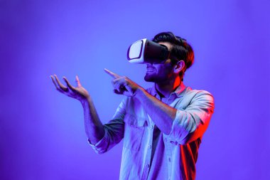 Sanal gerçeklik gözlüklü, sanal gerçeklikte hologram görüntüsü olan beyaz, zeki bir adam. Neon ışıklı arka planda gözlük ve kulaklık kullanarak bakıp işaret eden mutlu bir insan. Teknoloji. Sapma.
