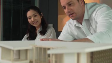 Ev planı çizmek için birlikte çalışan yetenekli mimar mühendisi. Mimar takımı, mimari model, plan ve dizüstü bilgisayarla ofis masasına yerleştirilen ev inşaatı hakkında tartışır. Yönlendirici.