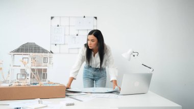 Genç, güzel beyaz bir mimar masanın üzerine plan koyar ve ev modeliyle karşılaştırırken, modern ofisteki fahişe modellerini dikkatlice incelerken arkadaki çizgilerle karşılaştırır. Tertemiz..