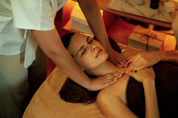 Caucasian woman customer enjoying relaxing anti-stress spa massage and pampering with beauty skin recreation leisure in warm candle lighting ambient salon spa at luxury resort or hotel. Quiescent