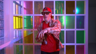 Komik break dansçı kameraya bakarken hiphop 'a doğru serbest adım atıyor. Çılgın mutlu hipster dans edip sokak dansı yaparken Led ışığında günlük kıyafet ve güneş gözlüğü takıyor. Mutluluk.