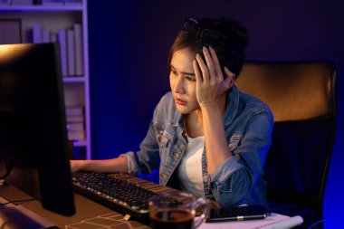 Stresli, genç, güzel Asyalı yaratıcı proje yaratıcısı sosyal medyayı araştırmak için bilgisayara bakıyor ve geceleri daha çok neon modern ofisin planlama kanalı stratejisine ulaşılıyor. Taktik.