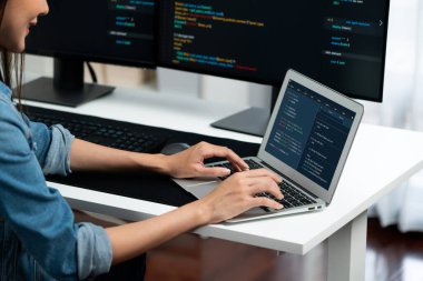 IT geliştiricisinde gülümseyen genç Asyalı dizüstü bilgisayarında kodlama programı verileriyle kotlu tişört giyerek çevrimiçi bilgi yazıyor. Güvenlik analizi iki ekran ile çevrili. Taktik.