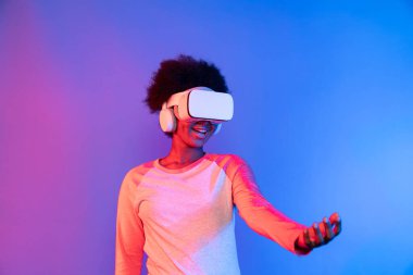 Genç Afrikalı, metaevren üzerinden VR gözlük takıyor ve elinde mavi pembe neon ışık grafikli dijital yenilik üzerine veri öğrenme uygulaması tutuyor. Entrika.